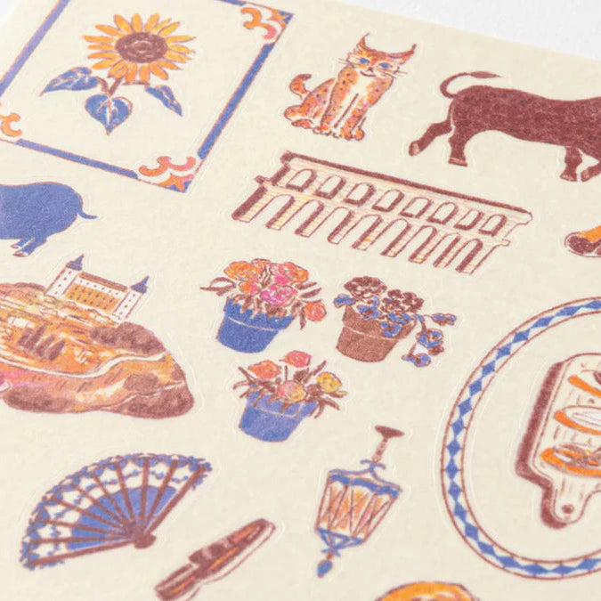 Patterned fabric with various illustrations including a sunflower, cat, bull, castle, flowers, and a fan on a beige background.