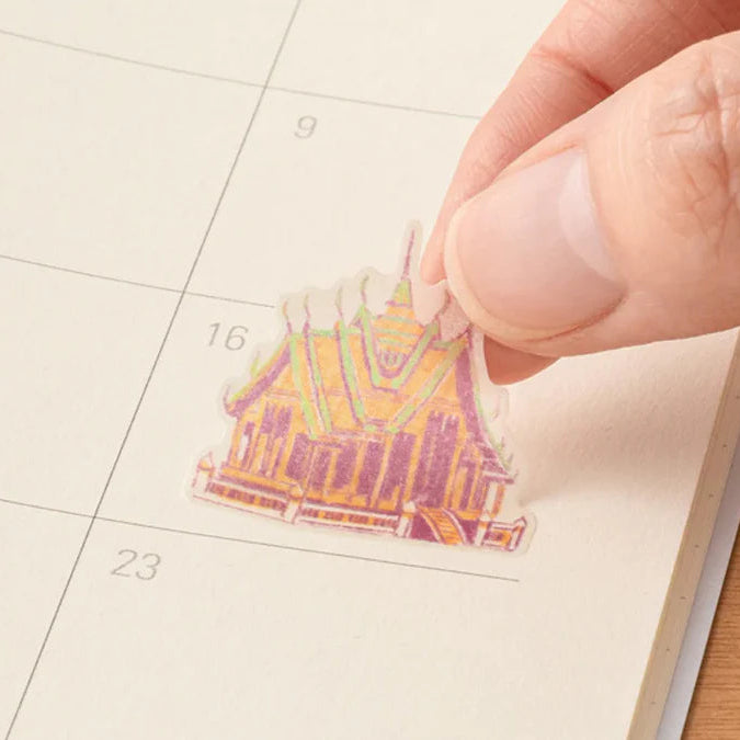 Hand placing a colorful sticker of a Thai temple on a calendar page