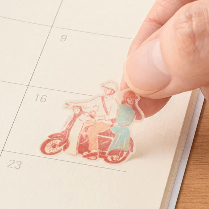 Small decorative sticker of a couple on a motorcycle held by a hand over a calendar.